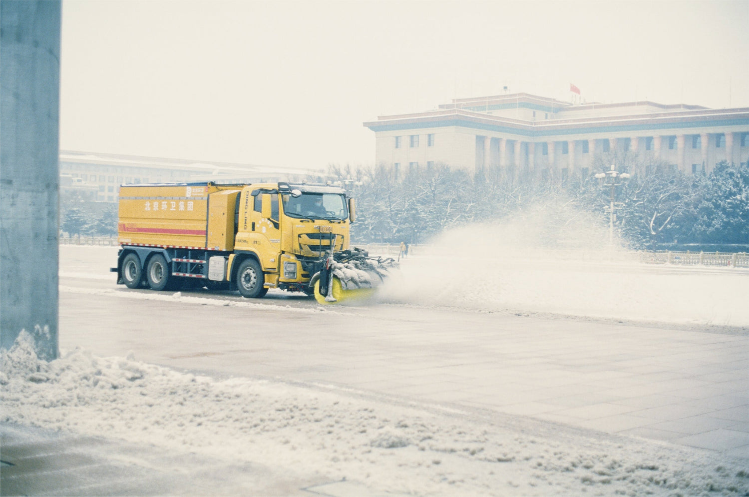 Snowplow clearing snow from the street in front of a government building, captured on KOMICHROME 100 slide film with medium grain.