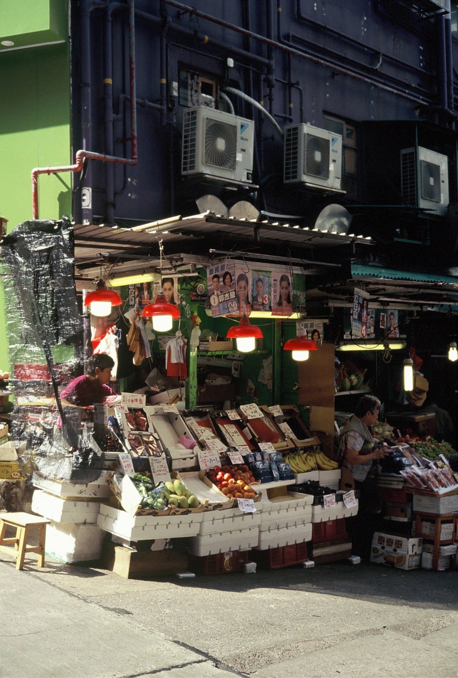 A bustling street market stall with fresh produce under red lanterns, captured on KOMICHROME 100 slide film with medium grain.