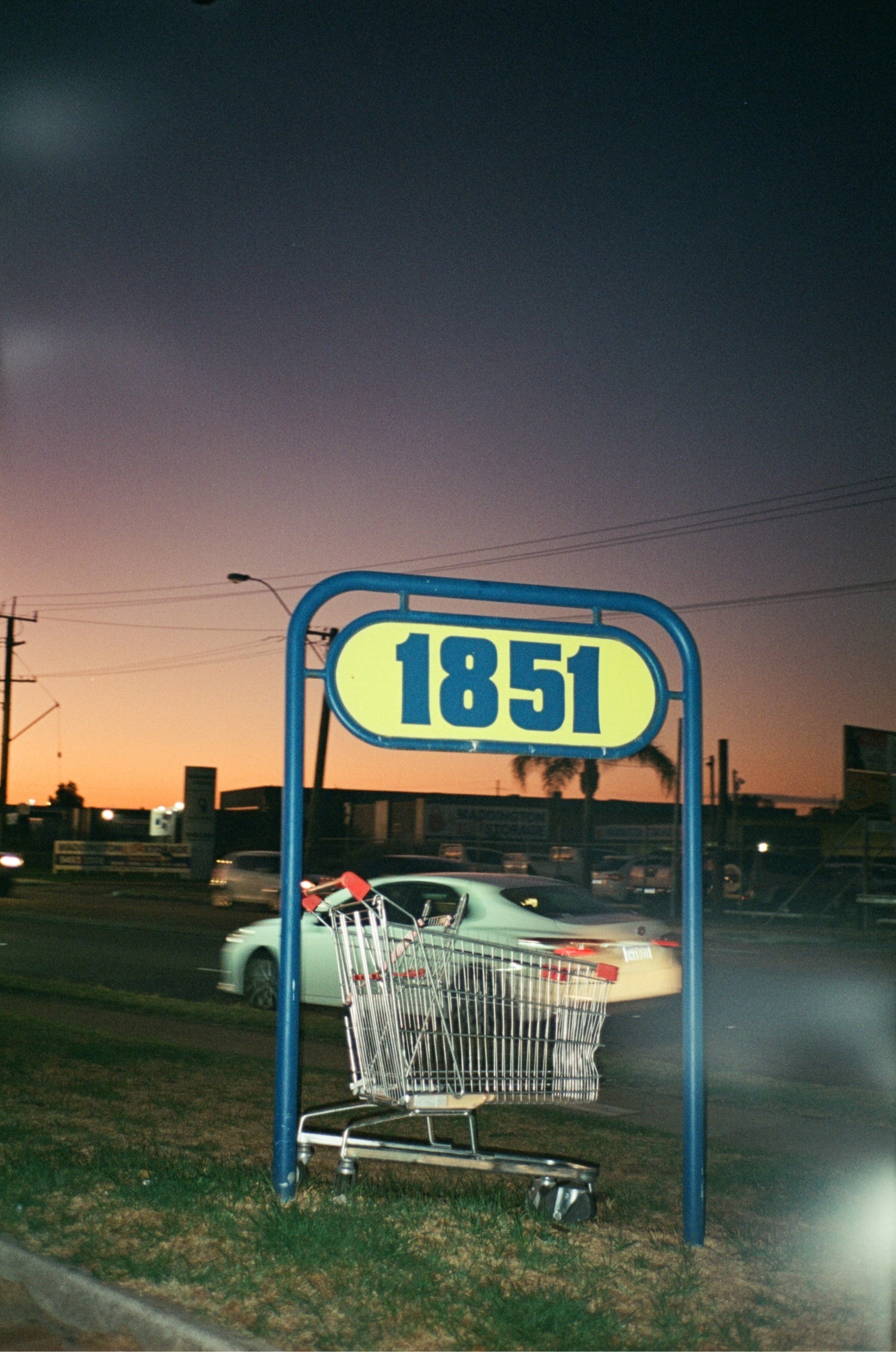 Shopping cart under a night sky with '1851' sign shot on MISO 200 film with medium grain